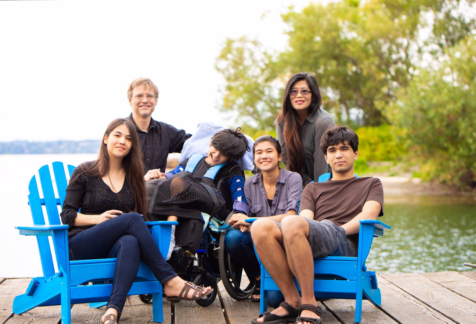 A family of six together on a lakeside dock, one son in a wheelchair