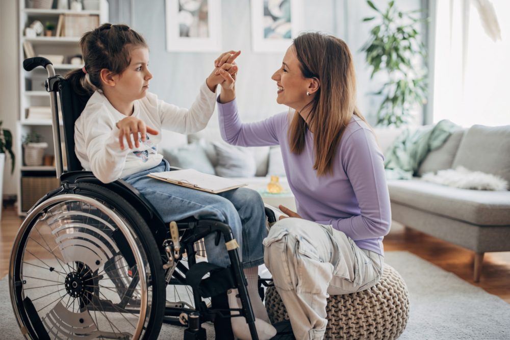 A mother and her daughter, who uses a wheelchair, playing together in their living room