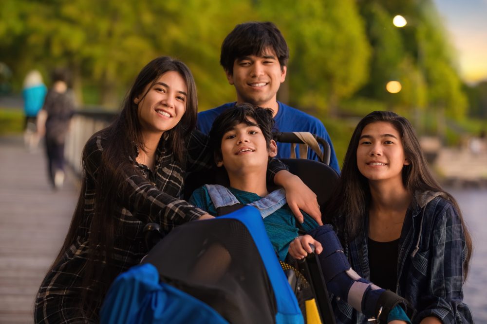 Four siblings on a boardwalk at dusk, the youngest in a wheelchair