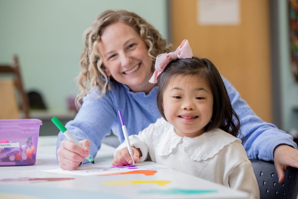 A teacher and a young girl drawing together at a table