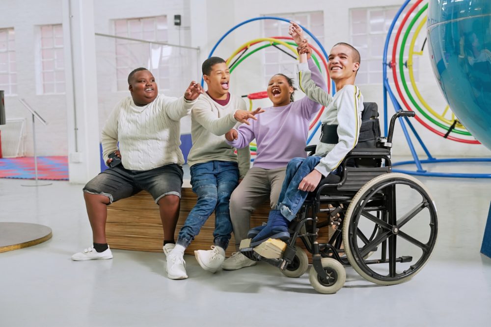 Four teenagers cheering together in a gym, one in a wheelchair