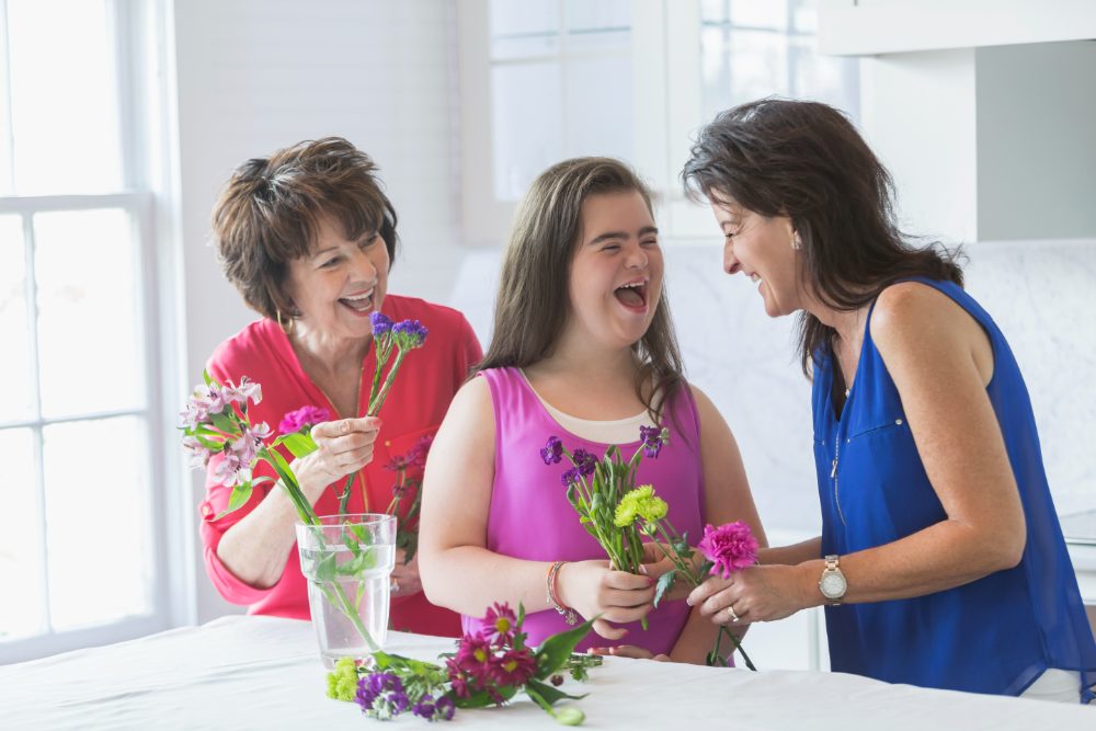 Three generations laughing while arranging flowers in a kitchen